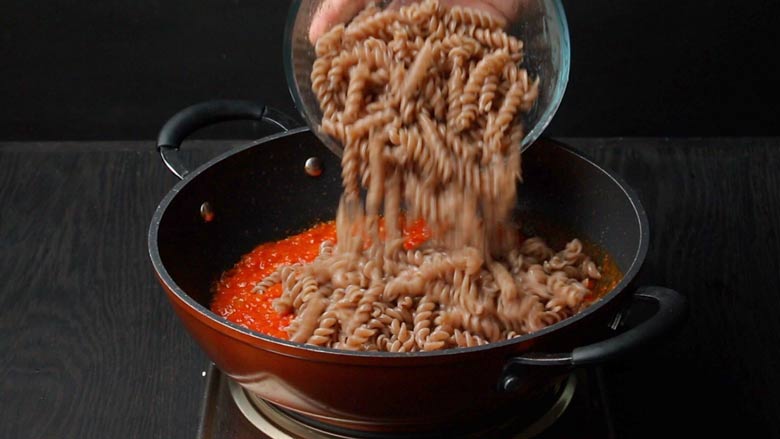 Boiled and drained pasta is added to the prepared marinara sauce in a non stick orange and black pan with two handles - Pizza Sauce Pasta Recipe