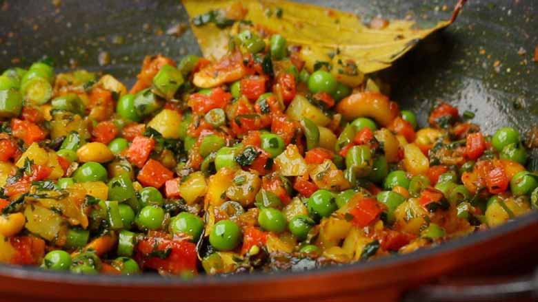 A colourful closeup shot of diced assorted vegetables being sautéed in a black and orange non stick kadhai - Semiya Pulao Recipe