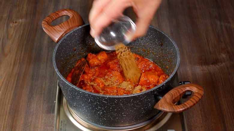 A hand is seen adding garam masala powder to the cooked soya chaap masala rogan josh style on an electric stove - Soya Chaap Curry Recipe