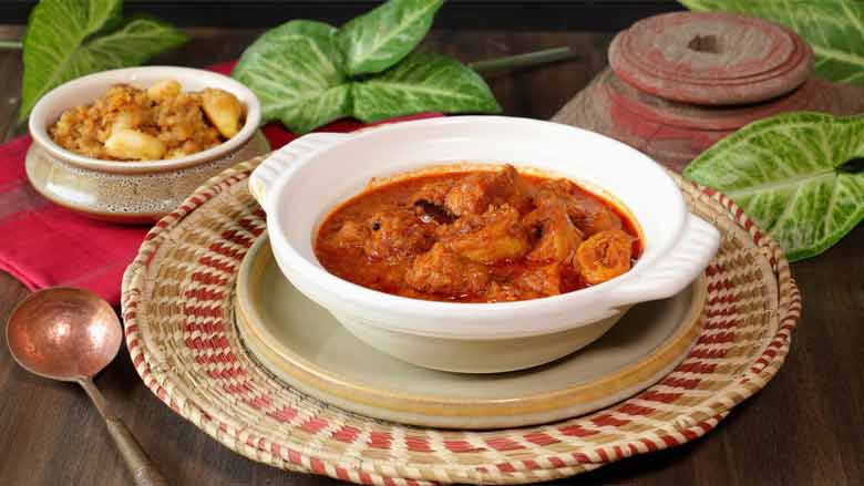 Soya chaap masala served and ready to eat in a shallow white ceramic bowl on a beige ceramic platter on a shallow handwoven basket with a copper ladle, dry potato dish, leaves, and an antique stand in the background - Soya Chaap Curry Recipe