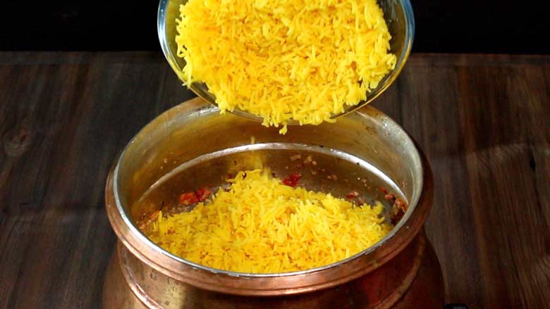 Cooked rice that is yellow in colour because of being cooked with turmeric is being tipped into a copper handi and layered over partially cooked chicken - Village Style Chicken Biryani Recipe